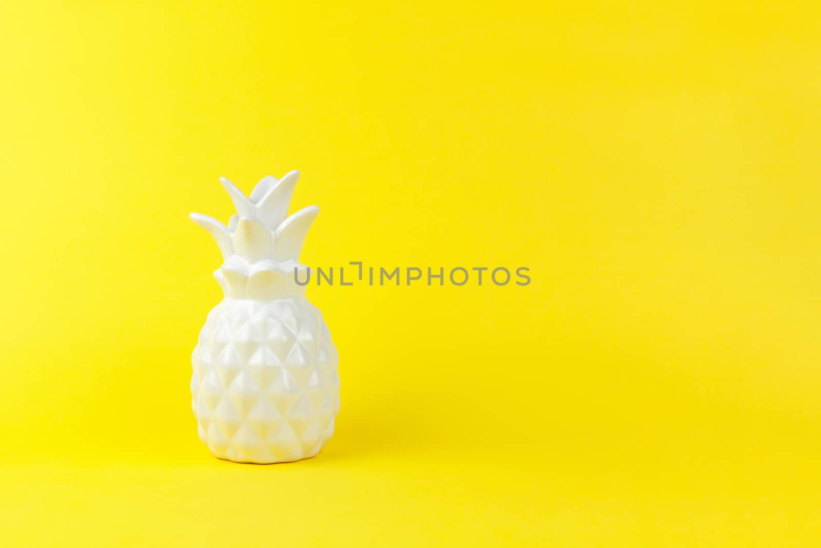 Trendy piece of interior white glossy ceramic pineapple on yellow paper background, copy space. Minimal style of decor concept. Horizontal. For lifestyle, interior blog, social media, poster.