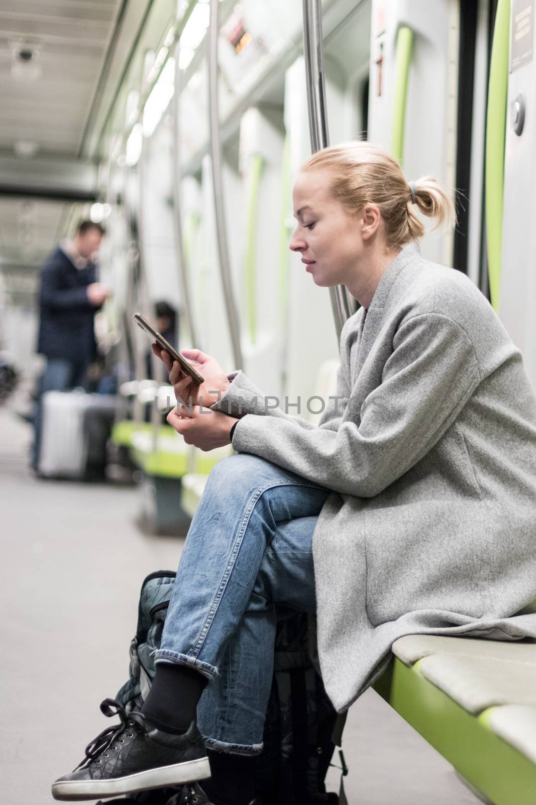 Portrait of lovely girl typing message on mobile phone in almost empty public subway train. Staying at home and social distancing recomented due to corona virus pandemic outbreak.