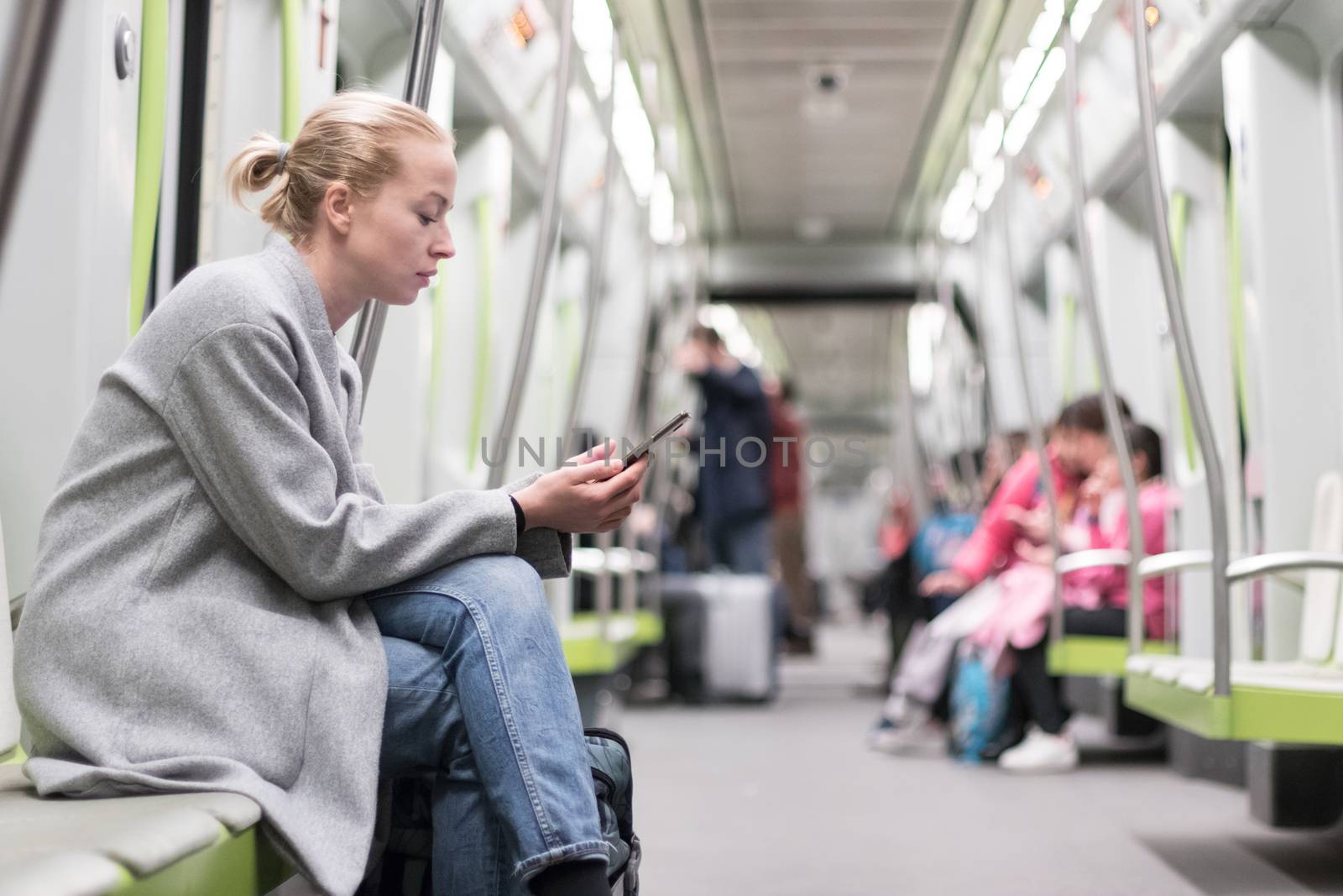 Portrait of lovely girl typing message on mobile phone in almost empty public subway train. Staying at home and social distancing recomented due to corona virus pandemic outbreak.