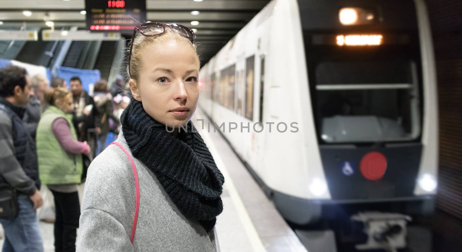 Young woman in winter coat going to work, waiting on the platform of a railway station for train to arrive. Public transport by kasto