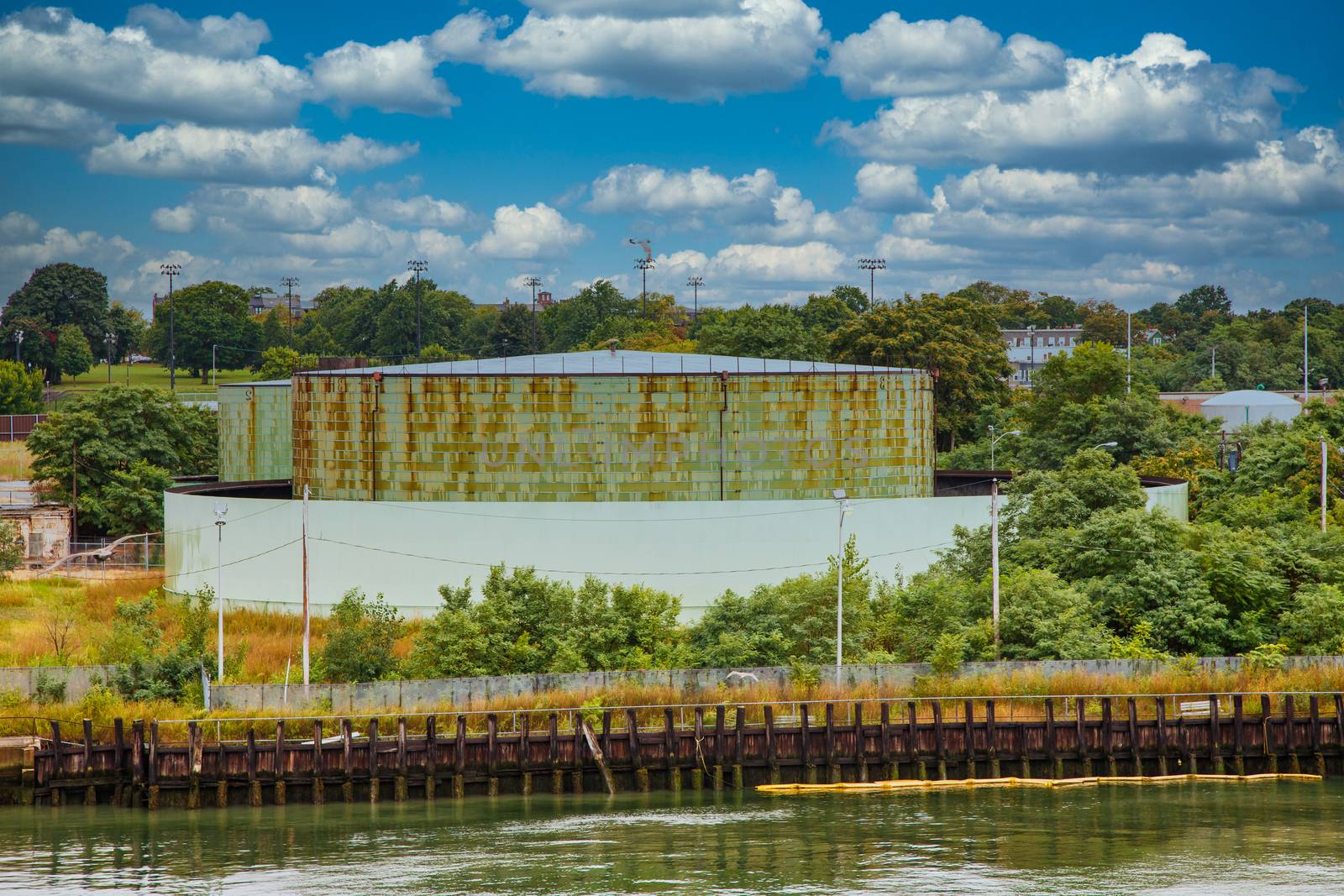 A large, round, green, metal water cistern on the edge of a canal