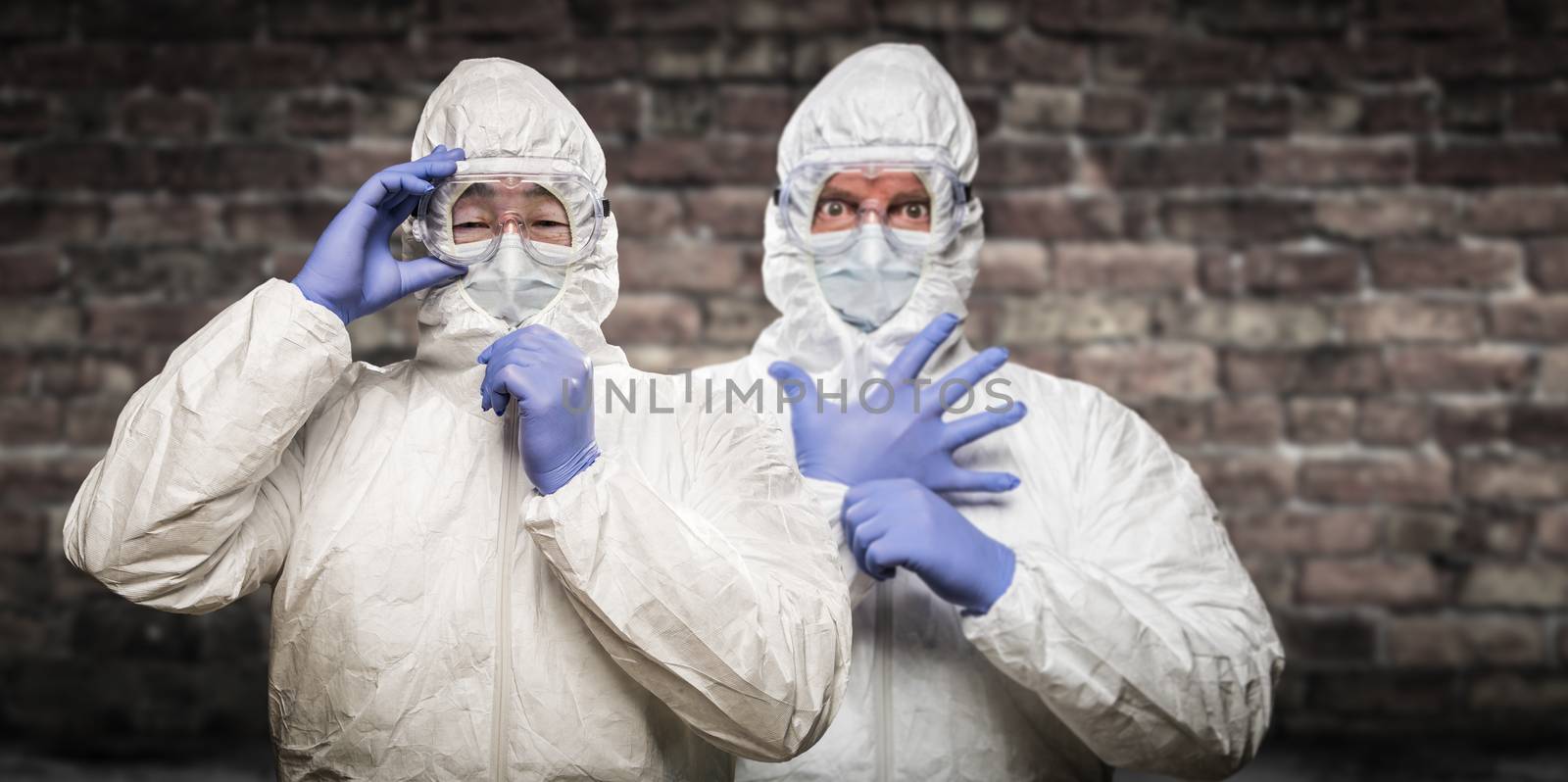 Chinese and Caucasian Men Wearing Hazmat Suit, Goggles and Mask with Brick Wall Background.