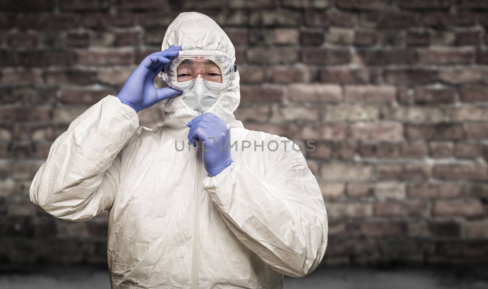 Chinese Man Wearing Hazmat Suit, Goggles and Mask with Brick Wall Background.