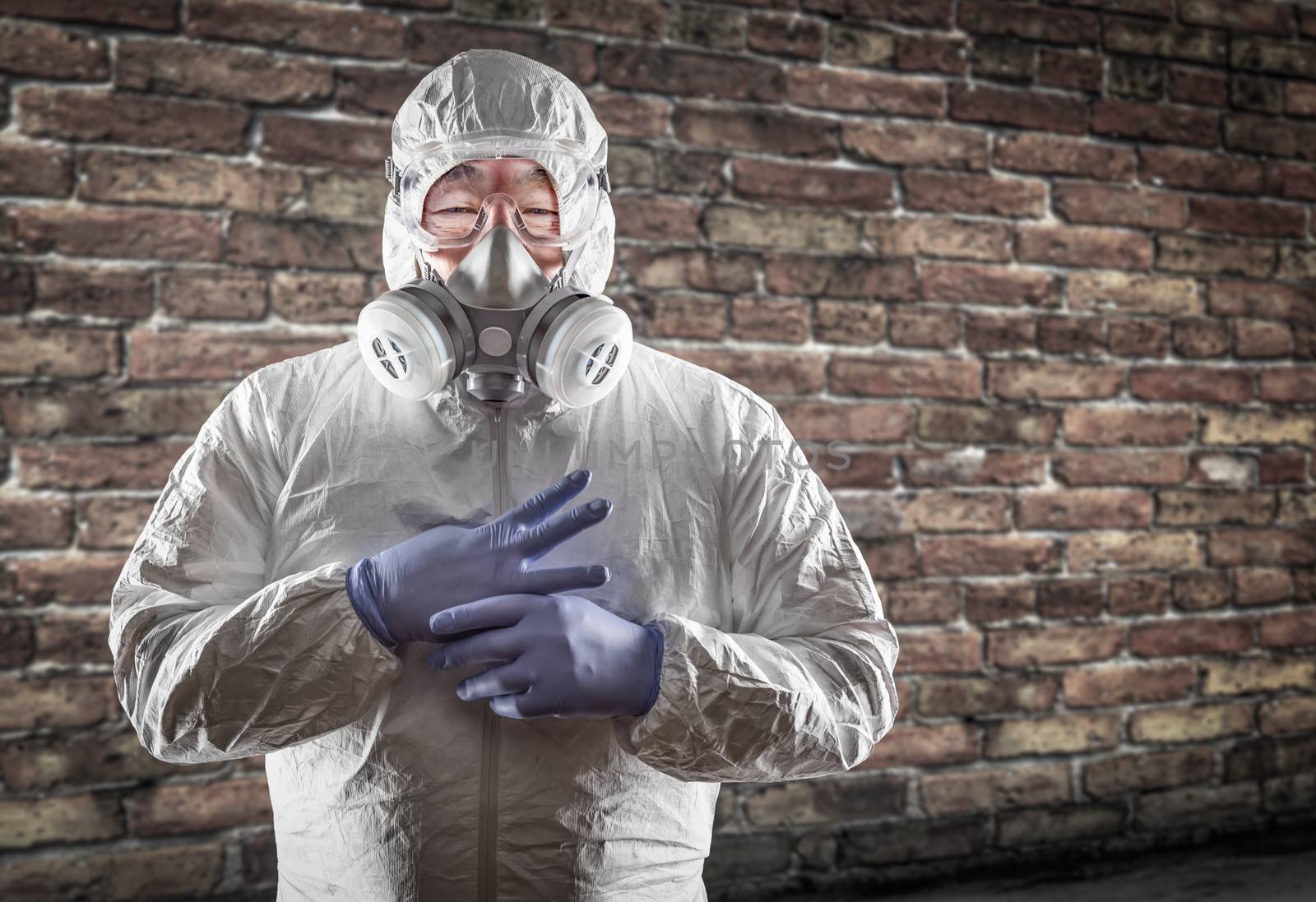 Chinese Man Wearing Hazmat Suit, Goggles and Gas Mask with Brick Wall Background.