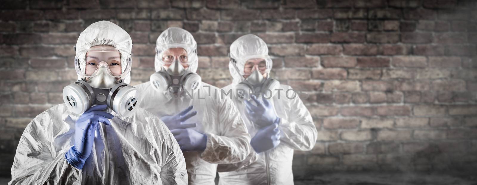 Chinese Woman and Team Behind In Hazmat Suites, Gas Masks and Goggles Against Brick Wall. by Feverpitched