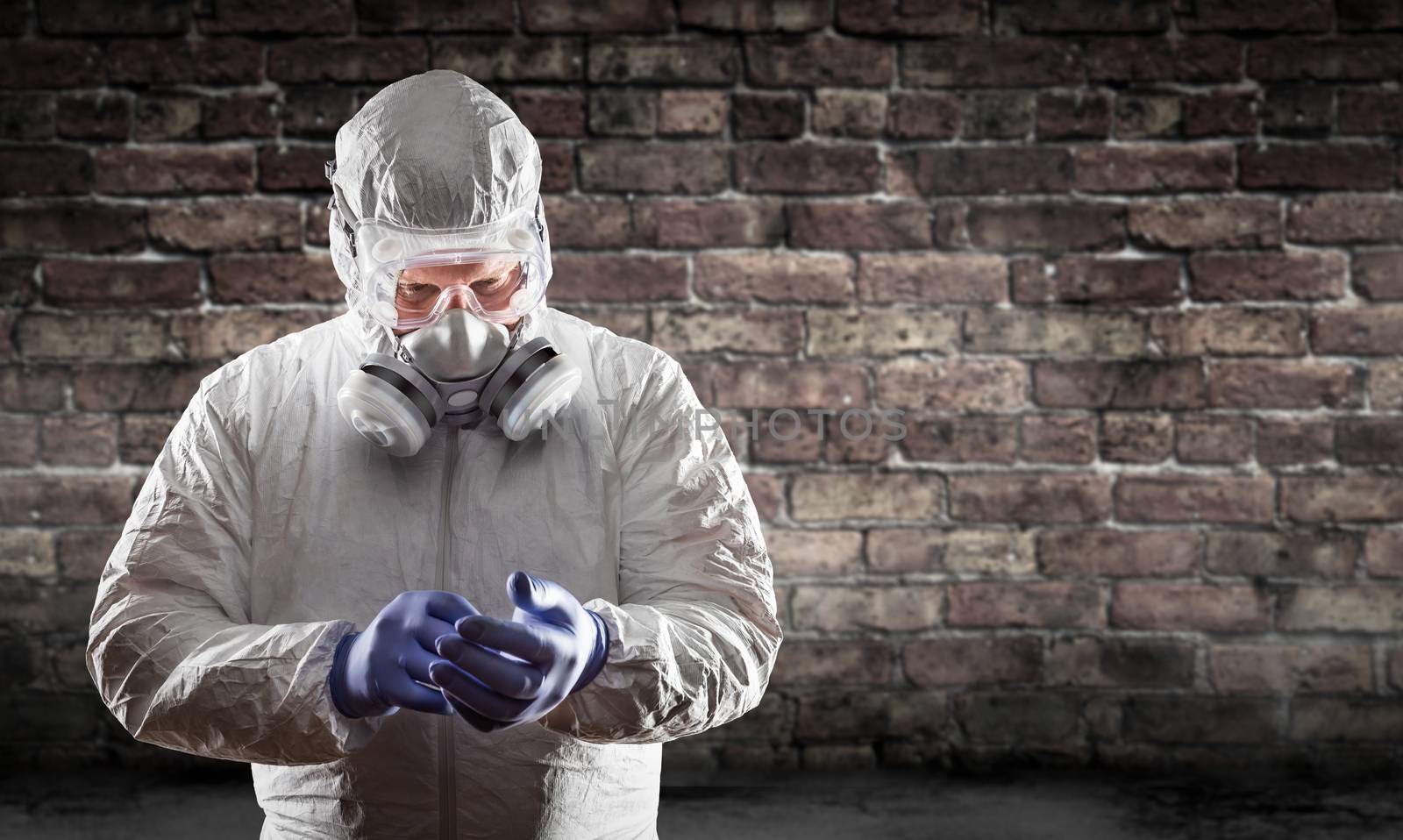 Man Wearing Hazmat Suit, Protective Gas Mask and Goggles Against Brick Wall.