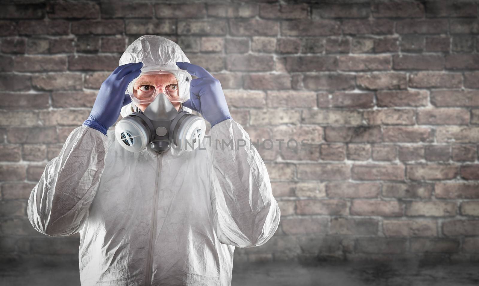 Man Wearing Hazmat Suit, Protective Gas Mask and Goggles Against Brick Wall