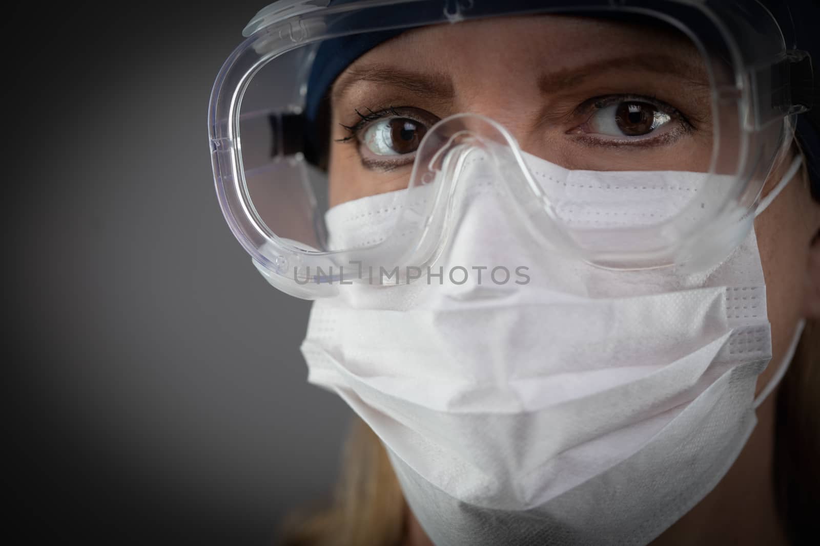 Female Medical Worker Wearing Protective Face Mask and Gear Against Dark Background.