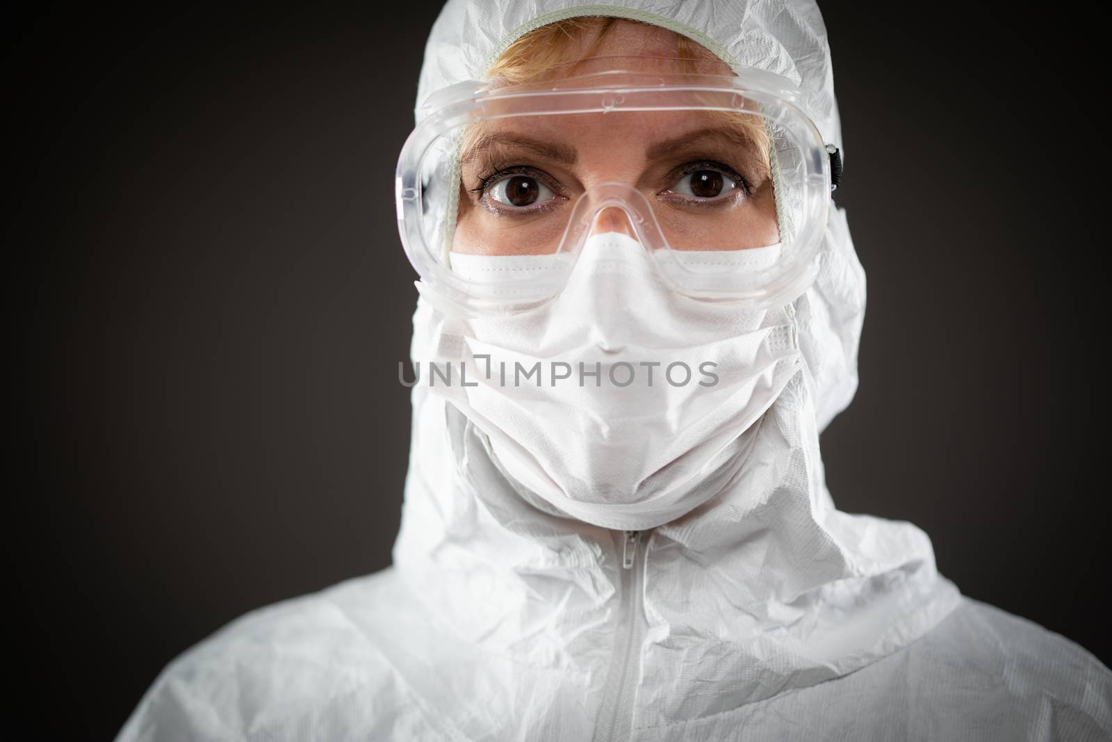 Female Medical Worker Wearing Protective Face Mask and Gear Against Dark Background. by Feverpitched