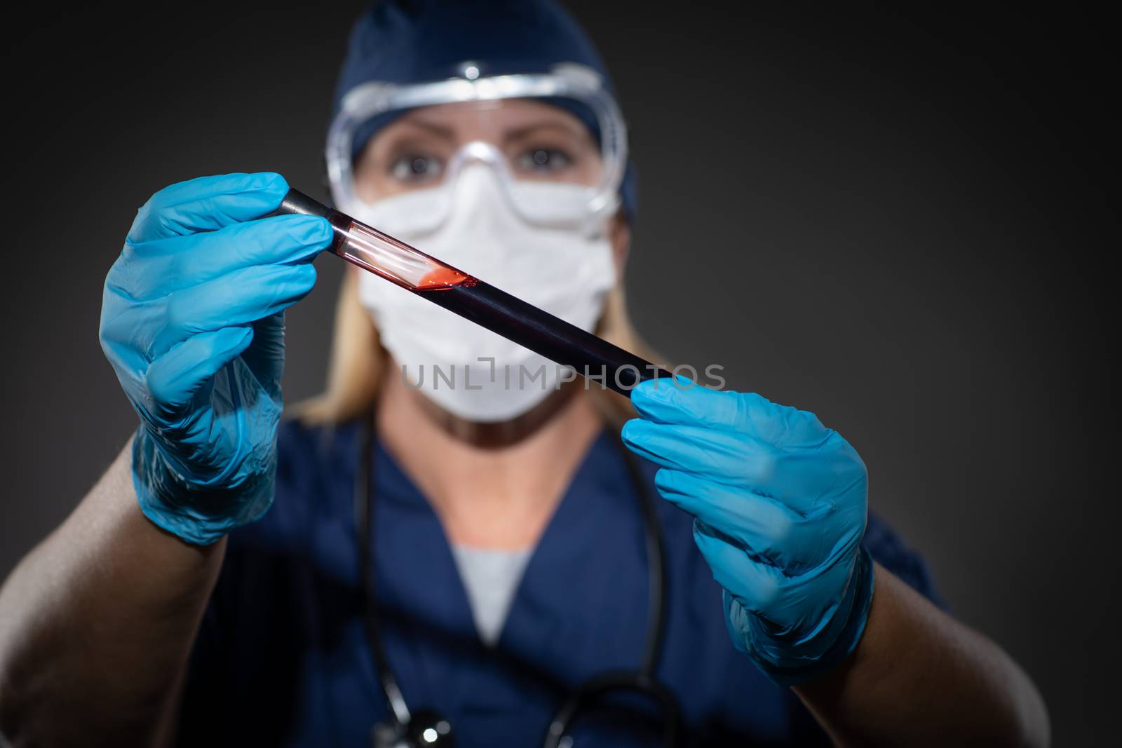 Female Lab Worker Wearing Medical Face Mask Holds Test Tube of Blood Against Dark Background. by Feverpitched