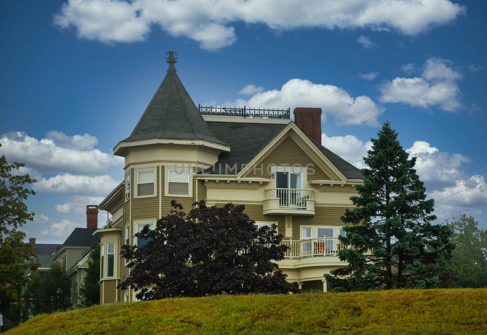 An old olive green victorian house on a grassy hill under foggy skies