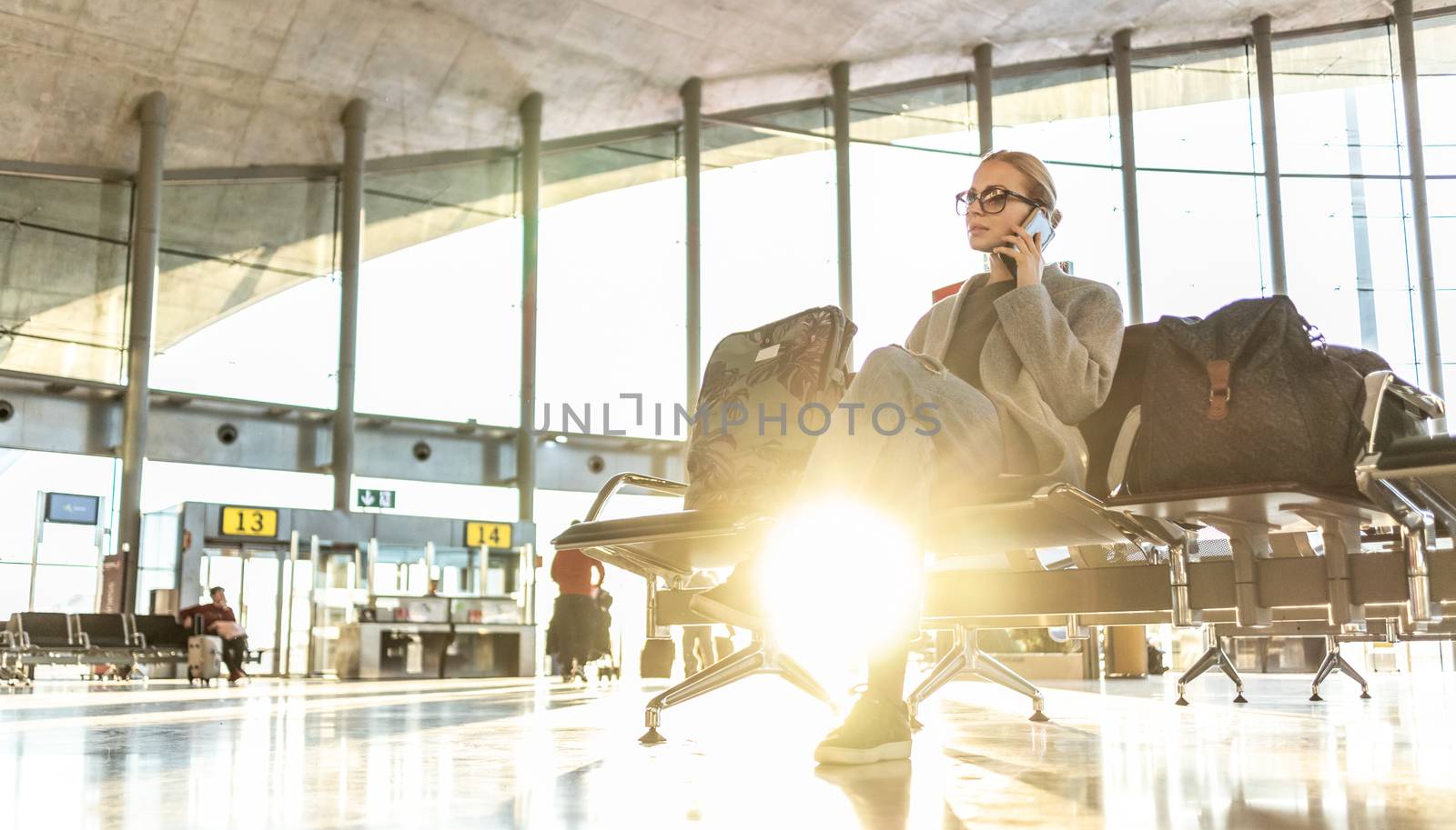 Casual blond young woman talking on cell phone while waiting to board a plane at airport departure gates.