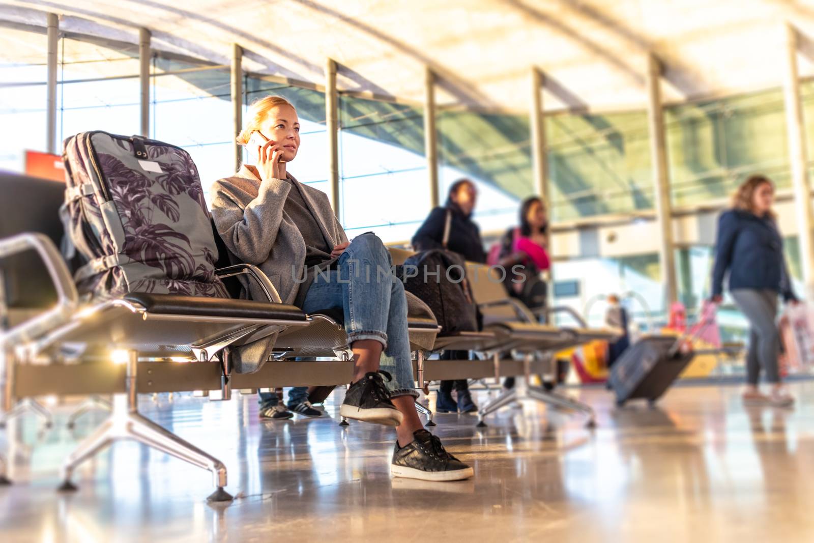 Casual blond young woman talking on cell phone while waiting to board a plane at bussy airport departure gates.