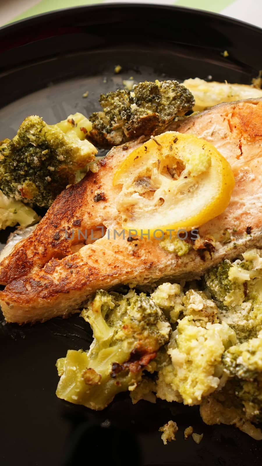 Top view of grilled salmon steak served on black plate with vegetable garnish from broccoli - vertical