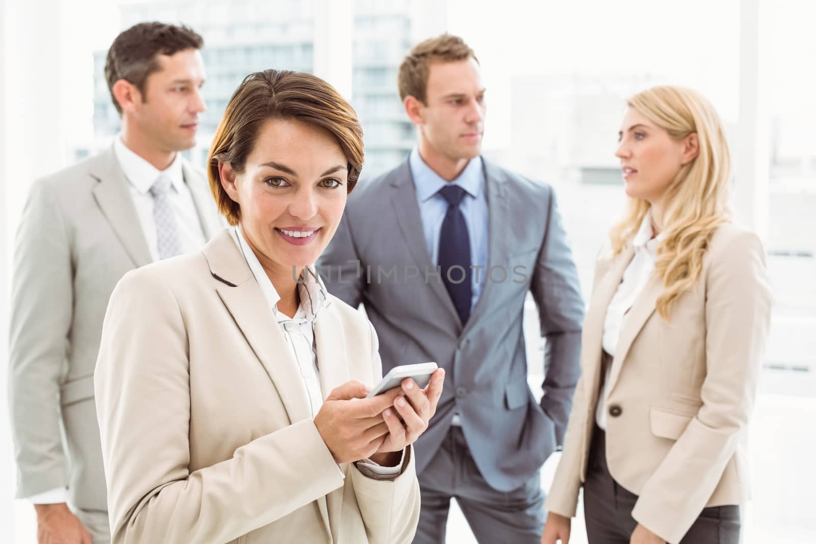 Businesswoman text messaging with colleagues in meeting behind by Wavebreakmedia