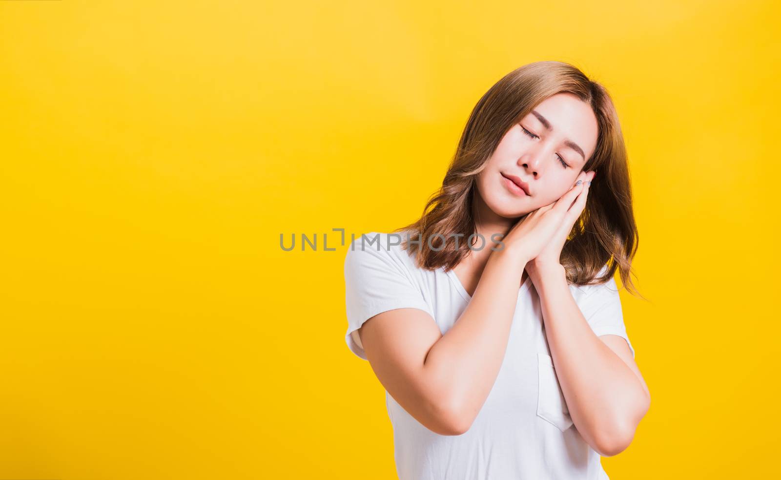 Portrait Asian Thai beautiful young woman emotions tired and sleepy her posing sleeping to dreaming with hands together near face, studio shot on yellow background, with copy space, insomnia concept
