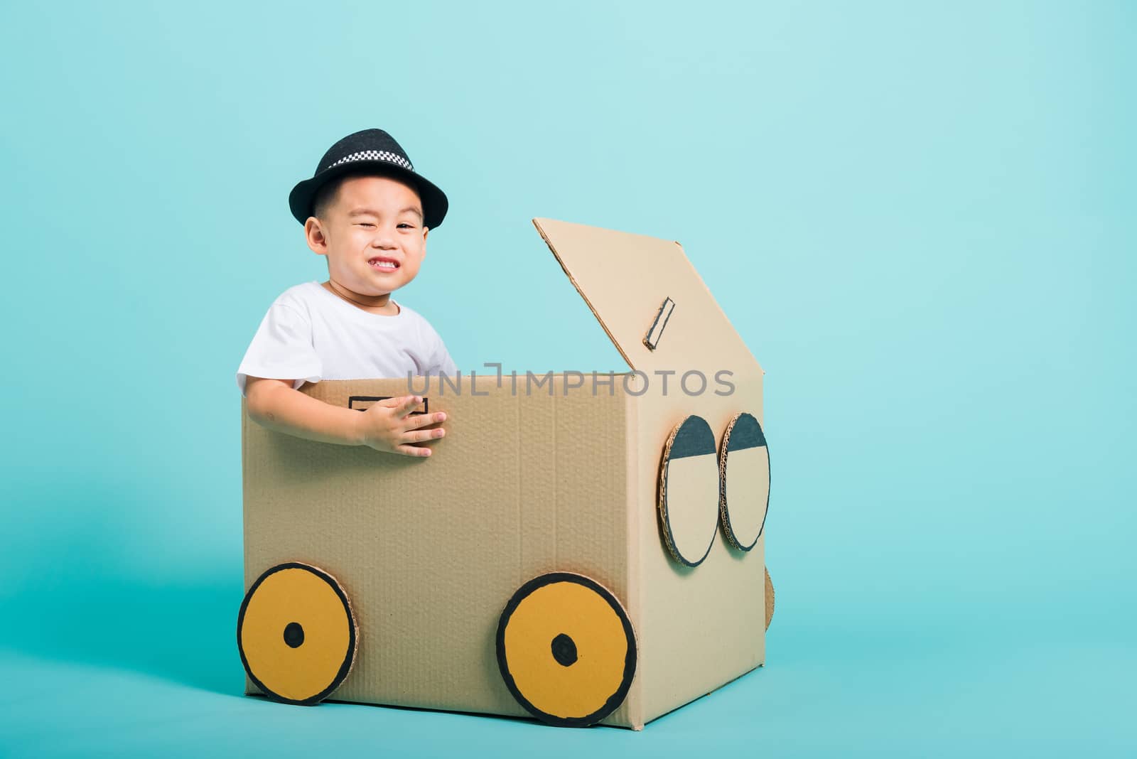 Happy Asian children boy smile in driving play car creative by a cardboard box imagination, summer holiday travel concept, studio shot on blue background with copy space for text