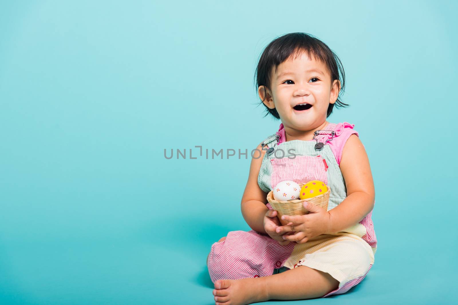 Asian Cute little baby girl beautiful holding Easter egg in basket, studio shot on blue background with copy space, Easter day concept