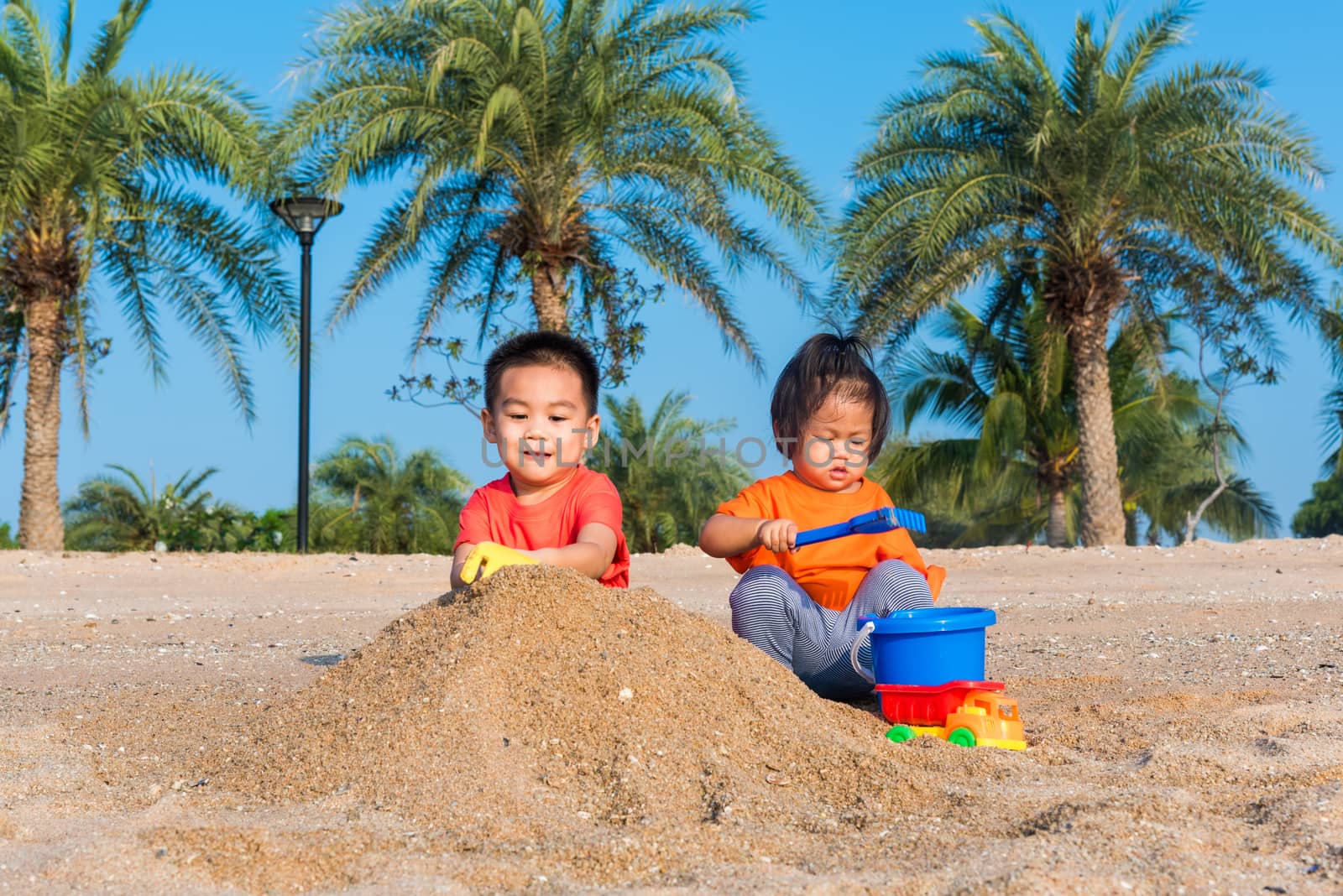 Asian Thai happy cute little cheerful Brother and sister two children funny digging play toy with sand at an outdoor tropical beach in summer day with copy space