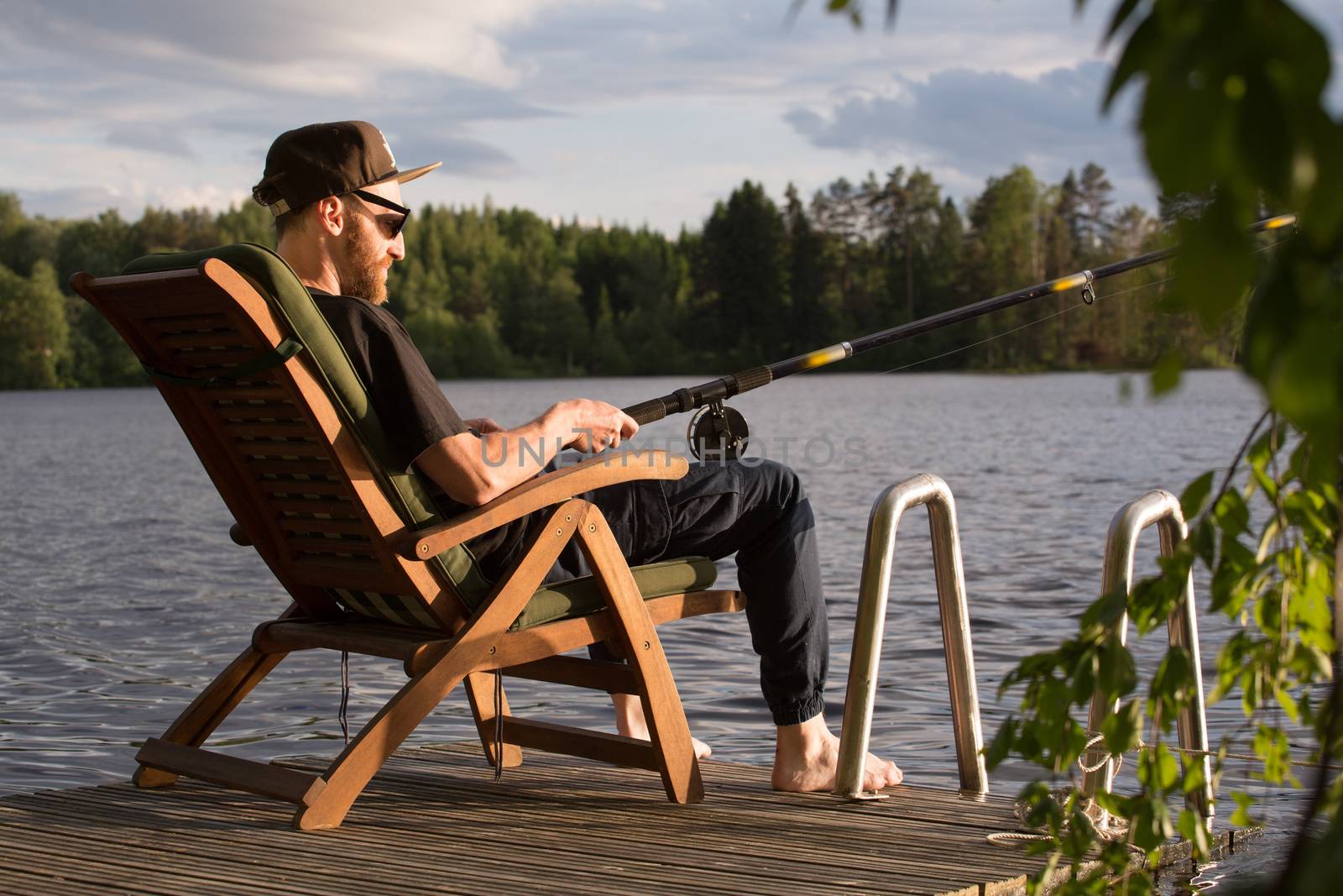 Mature man fishing from wooden pier near cottage on lake in Finland at summer