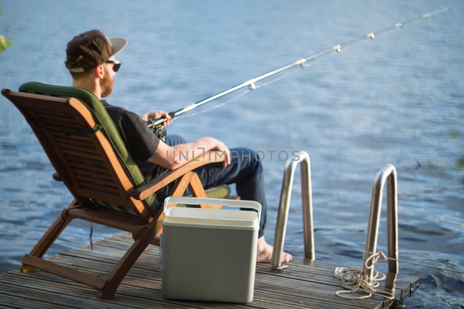 Mature man fishing from wooden pier near cottage on lake in Finland at summer