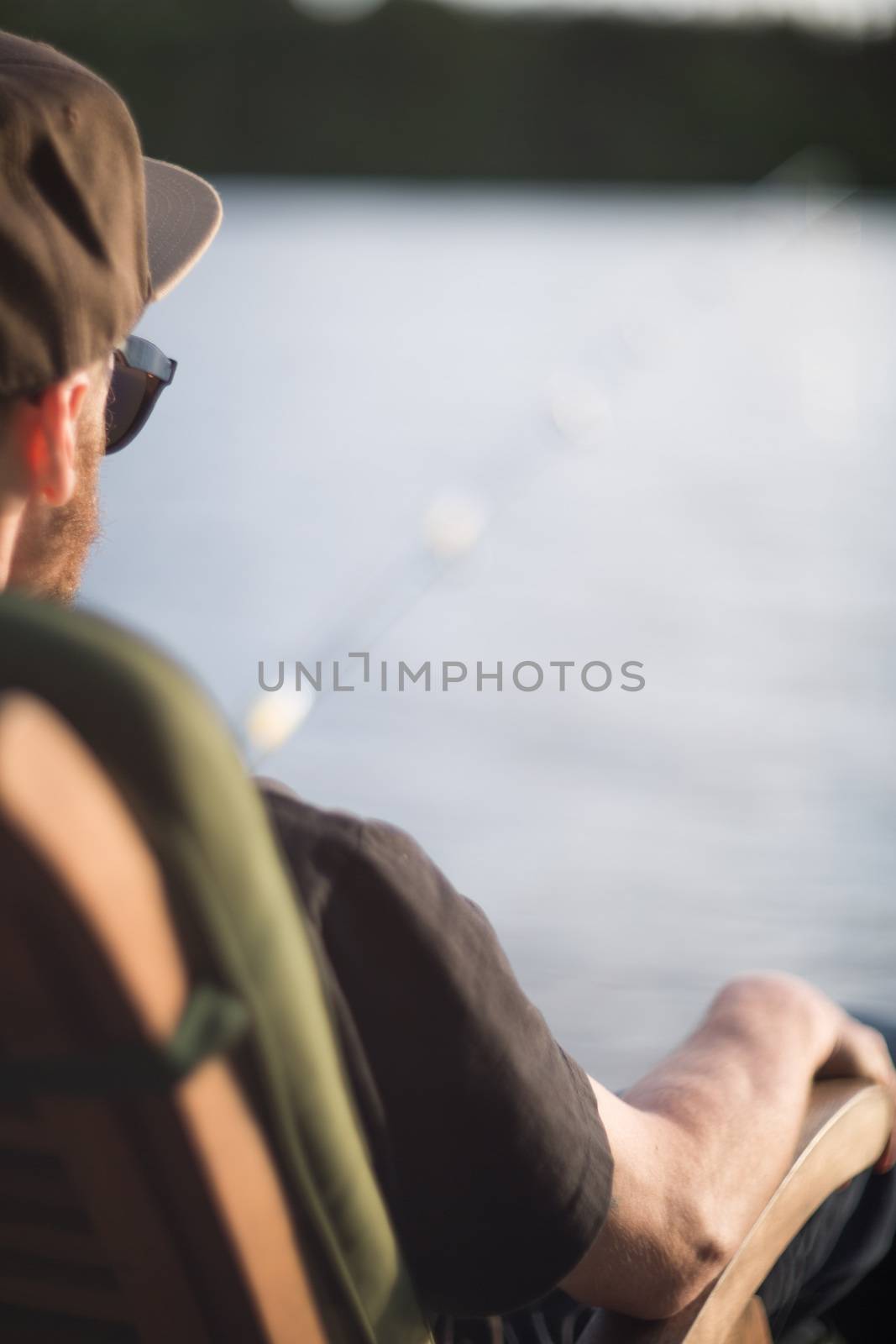 Mature man fishing from wooden pier near cottage on lake in Finland at summer