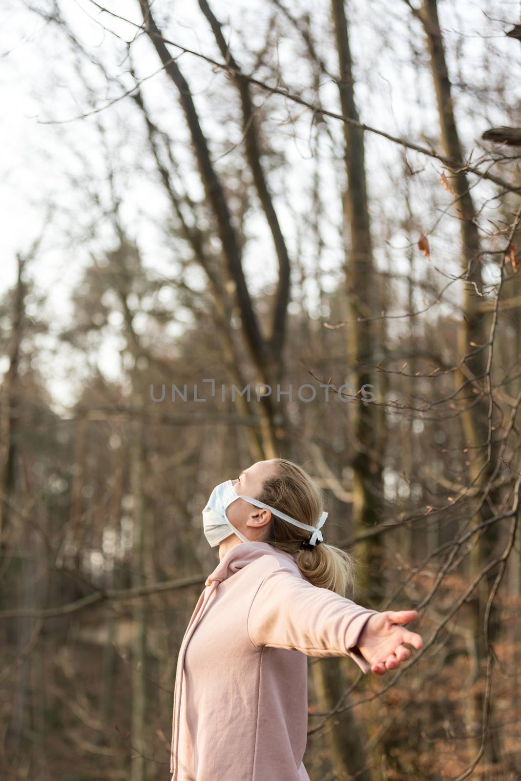 Portrait of caucasian sporty woman wearing medical protection face mask while relaxing by taking a deep breath in nature. Corona virus, or Covid-19, is spreading all over the world.