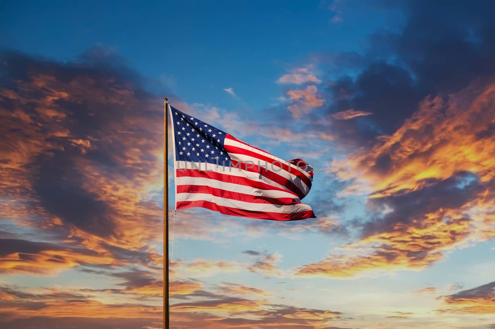 An American flag against a blue sky on an old rusty flagpole