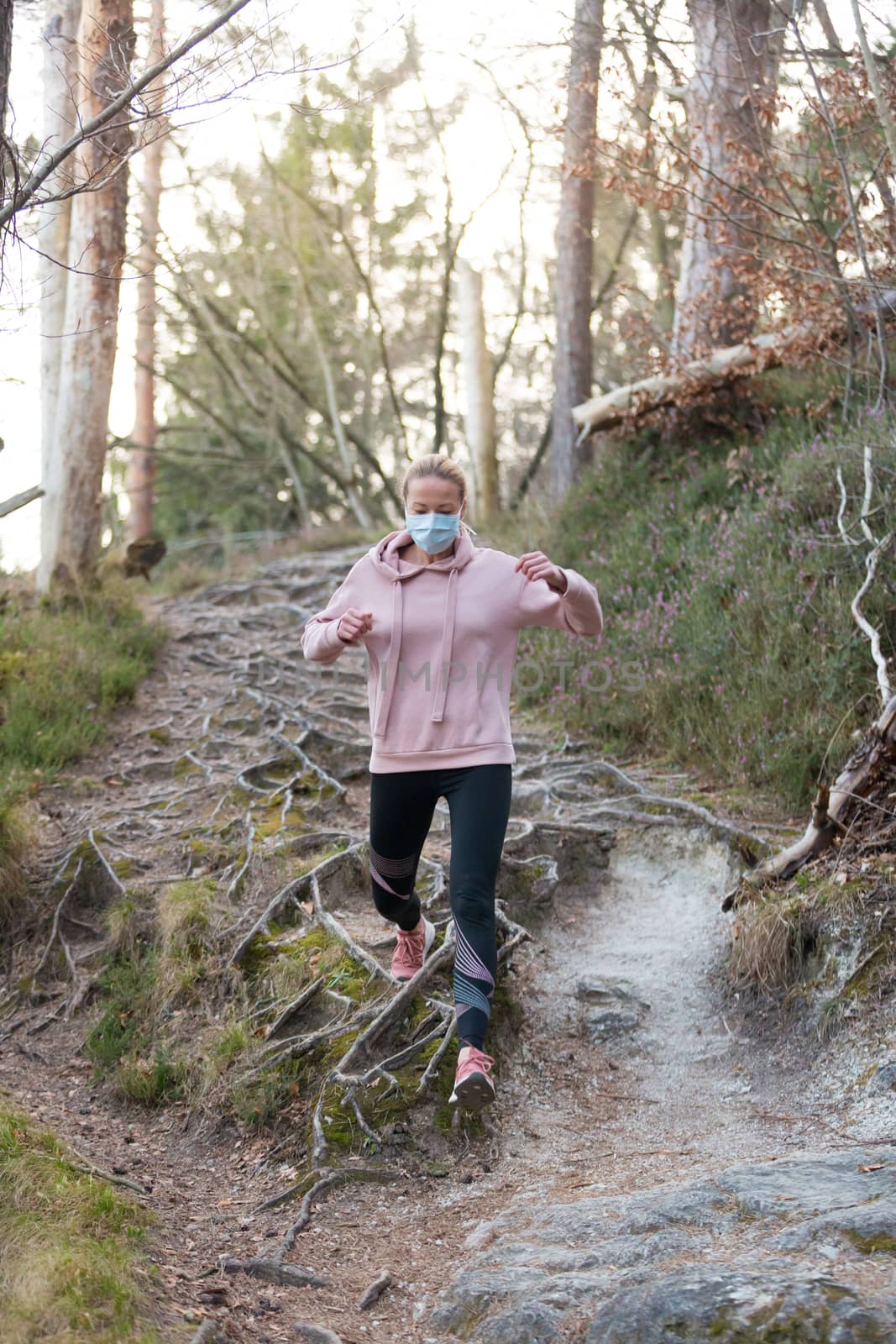 Corona virus, or Covid-19, is spreading all over the world. Portrait of caucasian sporty woman wearing a medical protection face mask while running in nature. by kasto