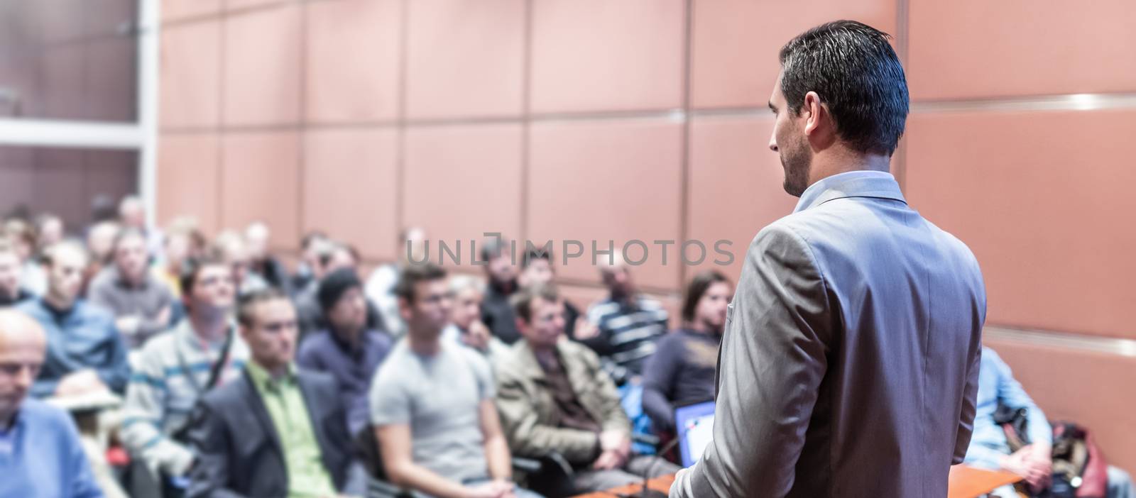 Speaker giving a talk on corporate business conference. Unrecognizable people in audience at conference hall. Business and Entrepreneurship event.