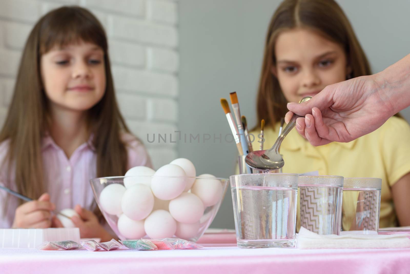 Mom pours vinegar in glasses of water for coloring eggs for Easter holidays