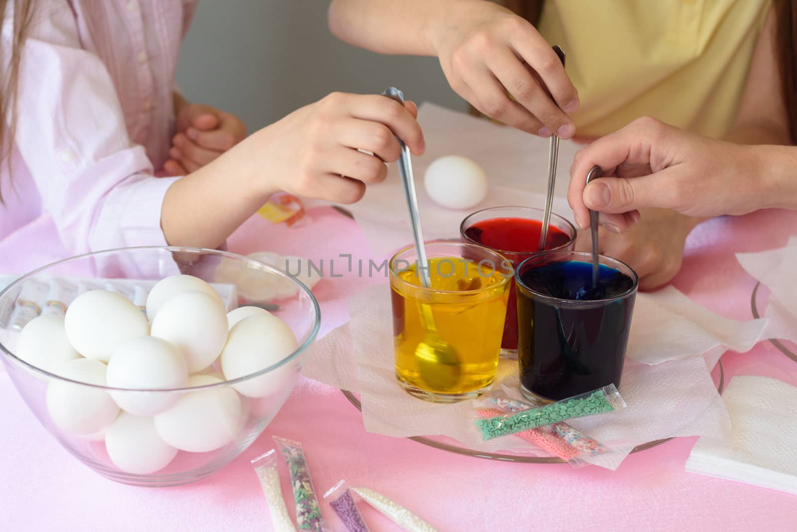 Children interfere with a solution with food coloring in glasses to paint Easter eggs by Madhourse