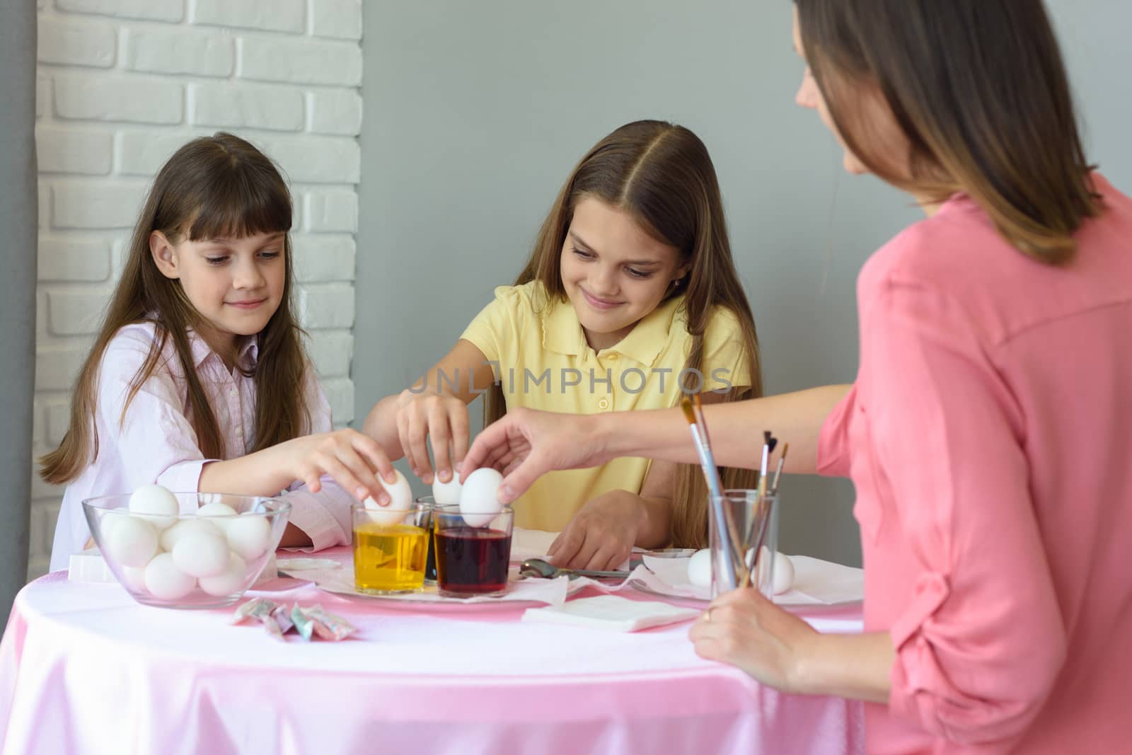 Children and mom dip chicken eggs in a dye solution