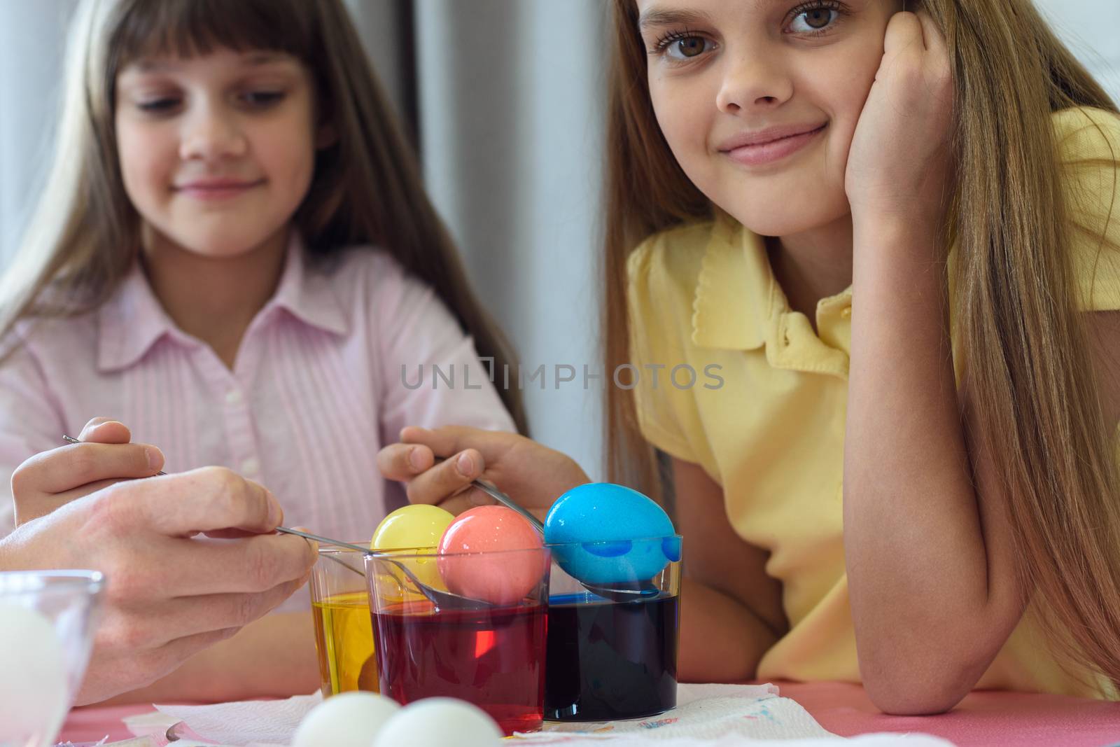 Coloring Easter eggs in glasses with liquid dye, the girl looked in the frame