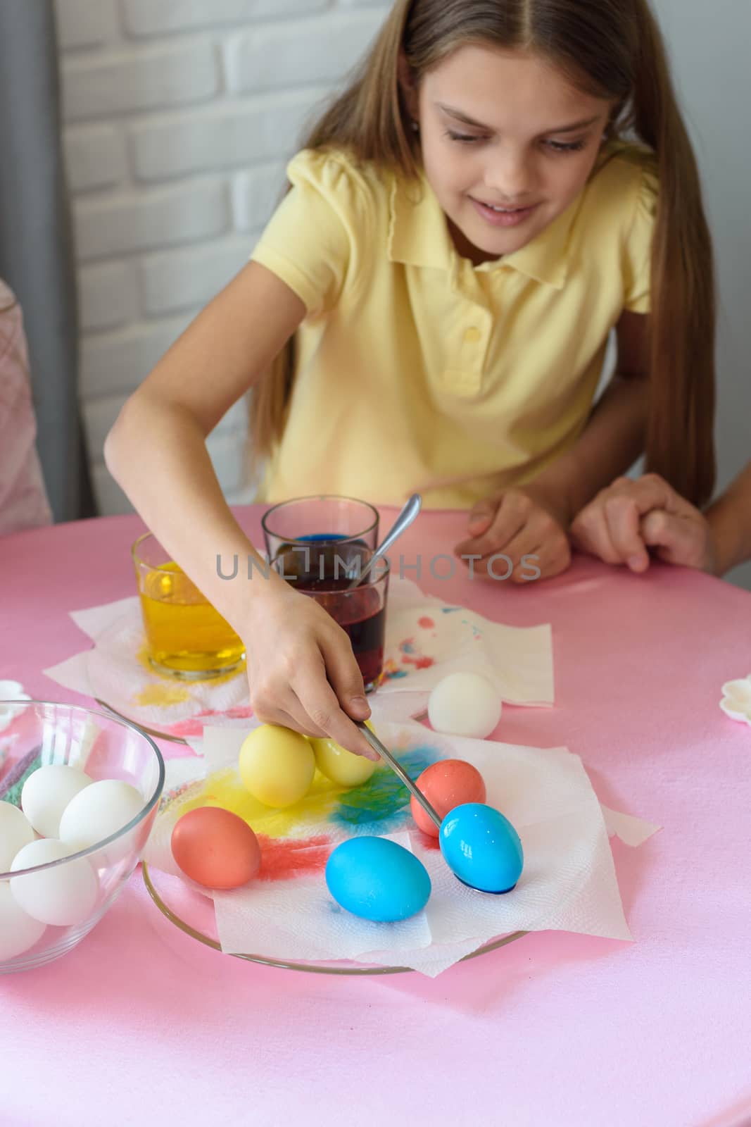 Girl paints Easter eggs in a special solution and puts on a plate by Madhourse