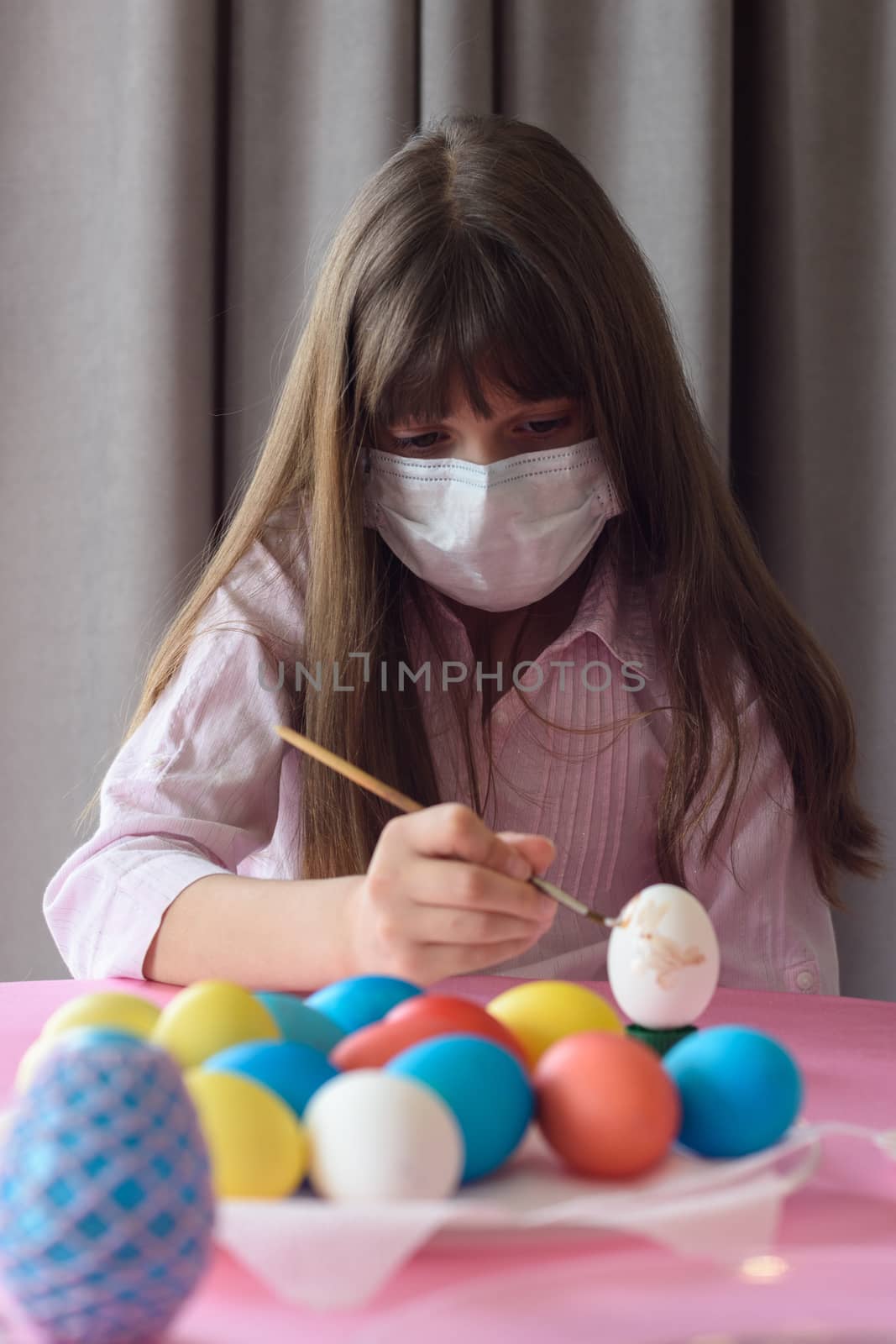 Sad quarantined girl paints Easter eggs with a brush