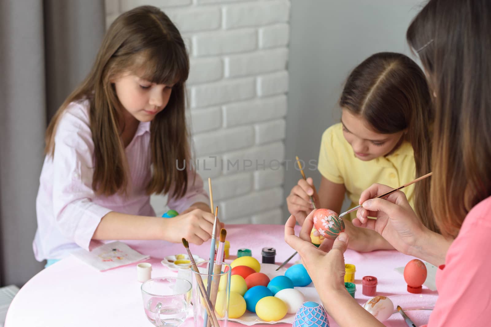 Mom and daughters enthusiastically paint Easter eggs at home