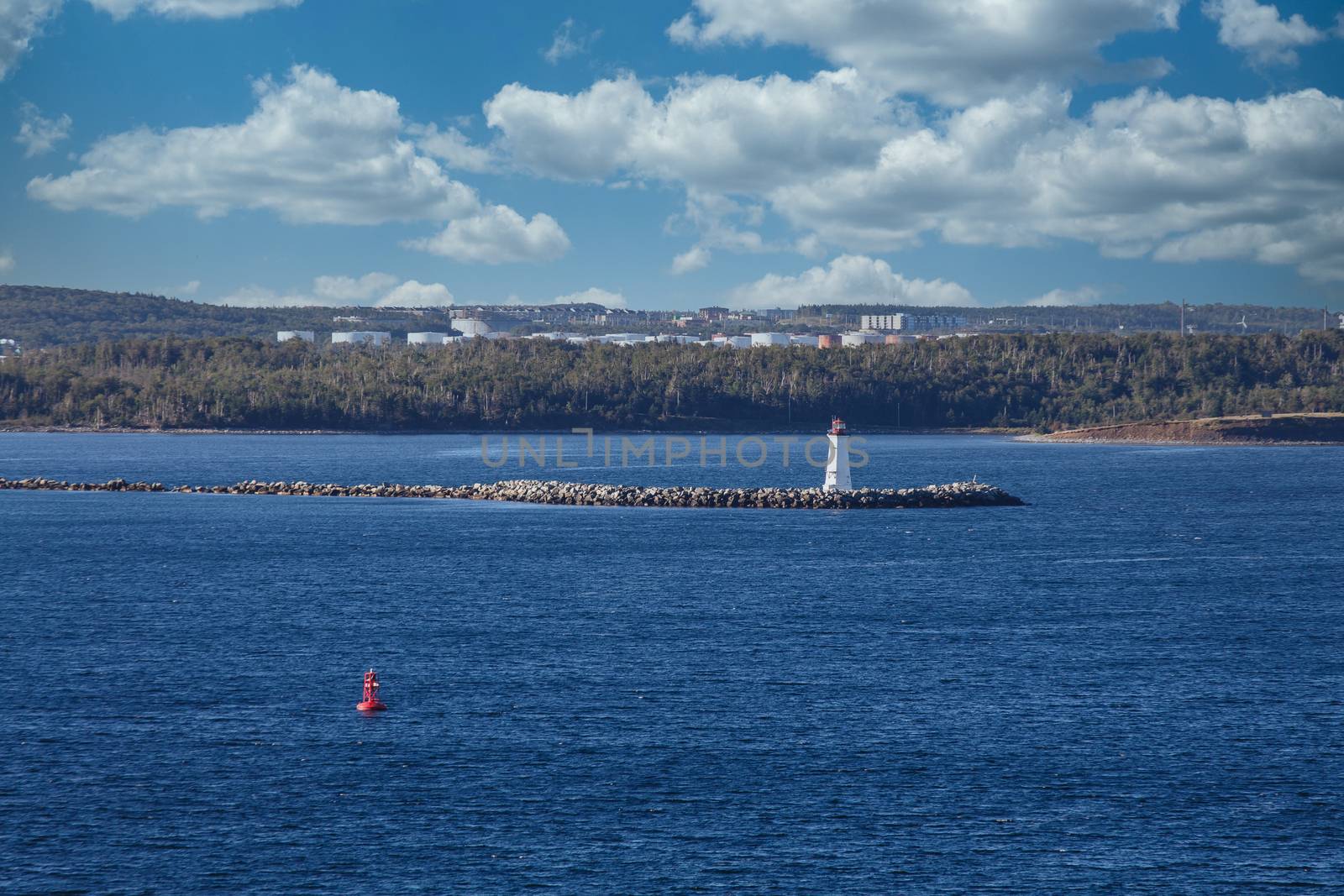 Small red and white lighthouse on point of seawall near a red channel marker in deep blue water