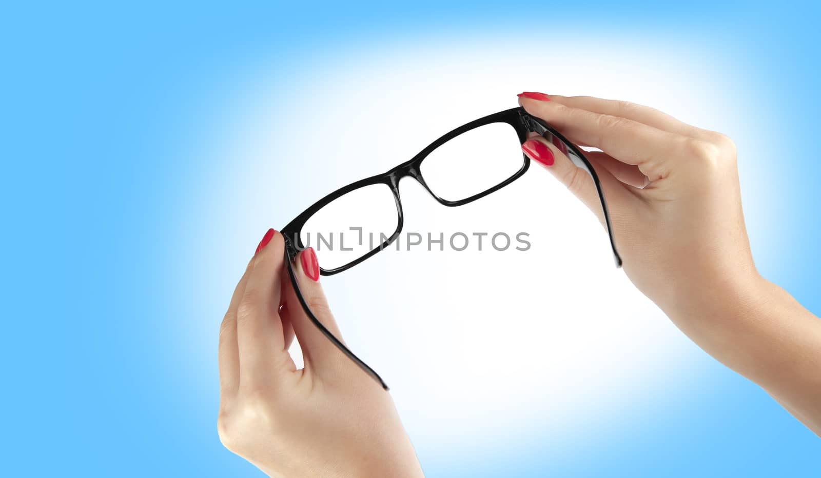 Female hand holding a black-framed glasses isolated on blue back by SlayCer