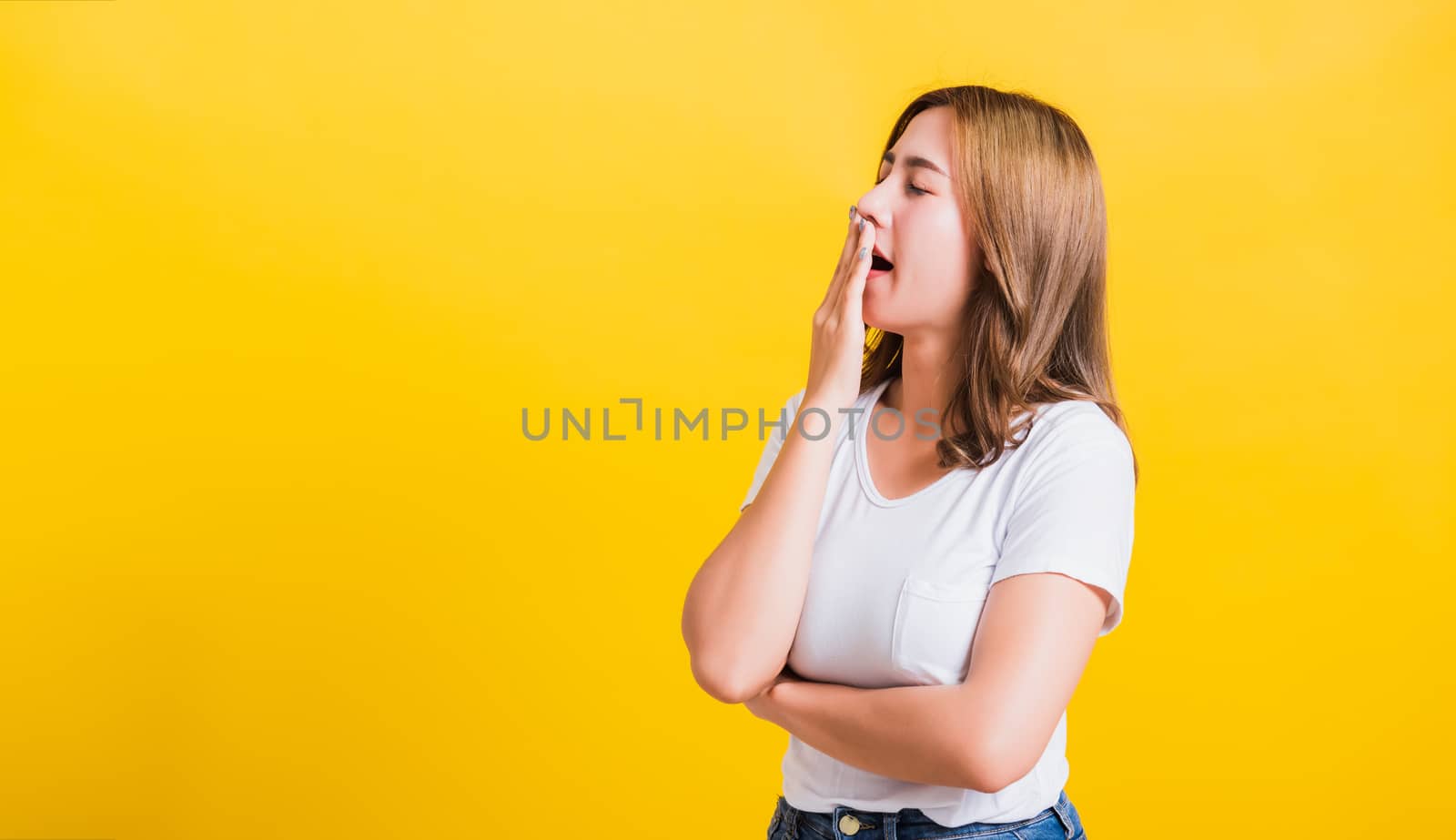 Portrait Asian Thai beautiful young woman emotions tired and sleepy her yawning close mouth open by hand, shoot a photo in the studio on yellow background, There was copy space, insomnia concept