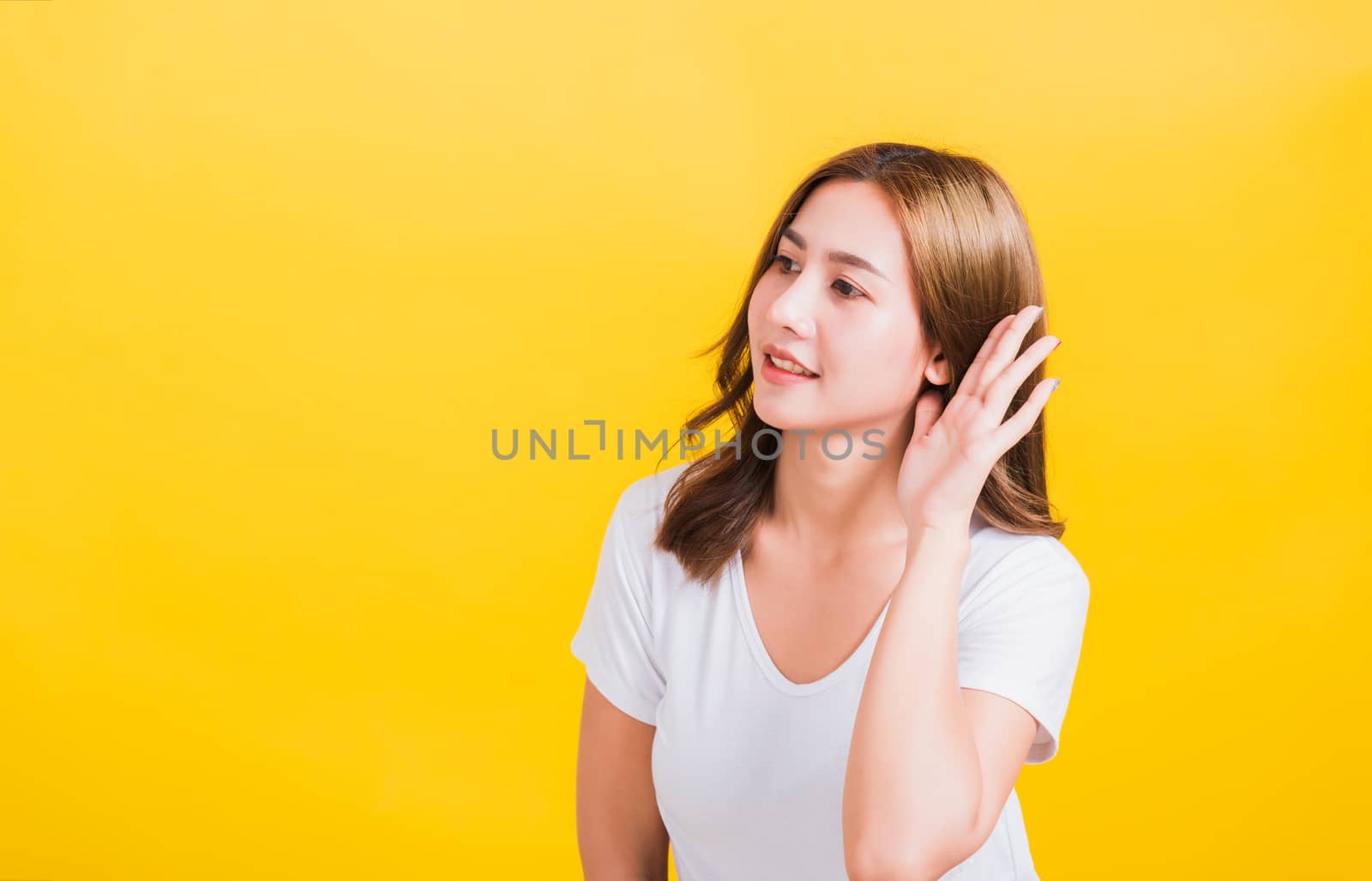 Portrait Asian Thai beautiful young woman listening something with her palm hand behind the ear, studio shot isolated on yellow background, There was copy space, Gossip concept