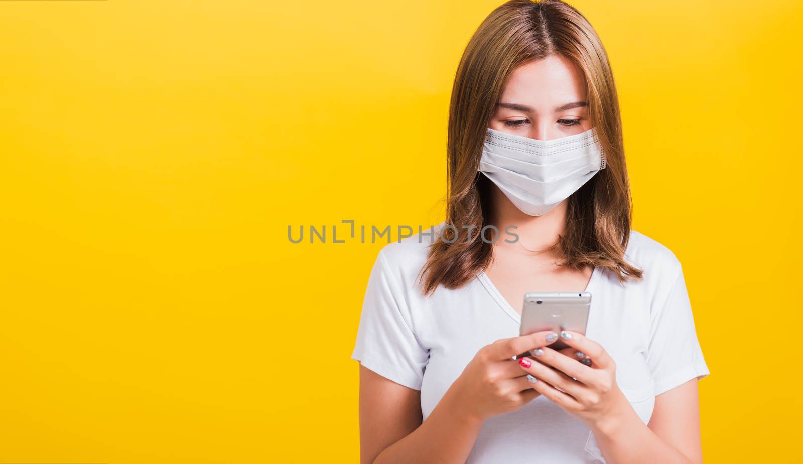 Portrait Asian Thai beautiful happy young woman wearing mask protection, reading news update on smartphone health care, studio shot isolated on yellow background, with copy space