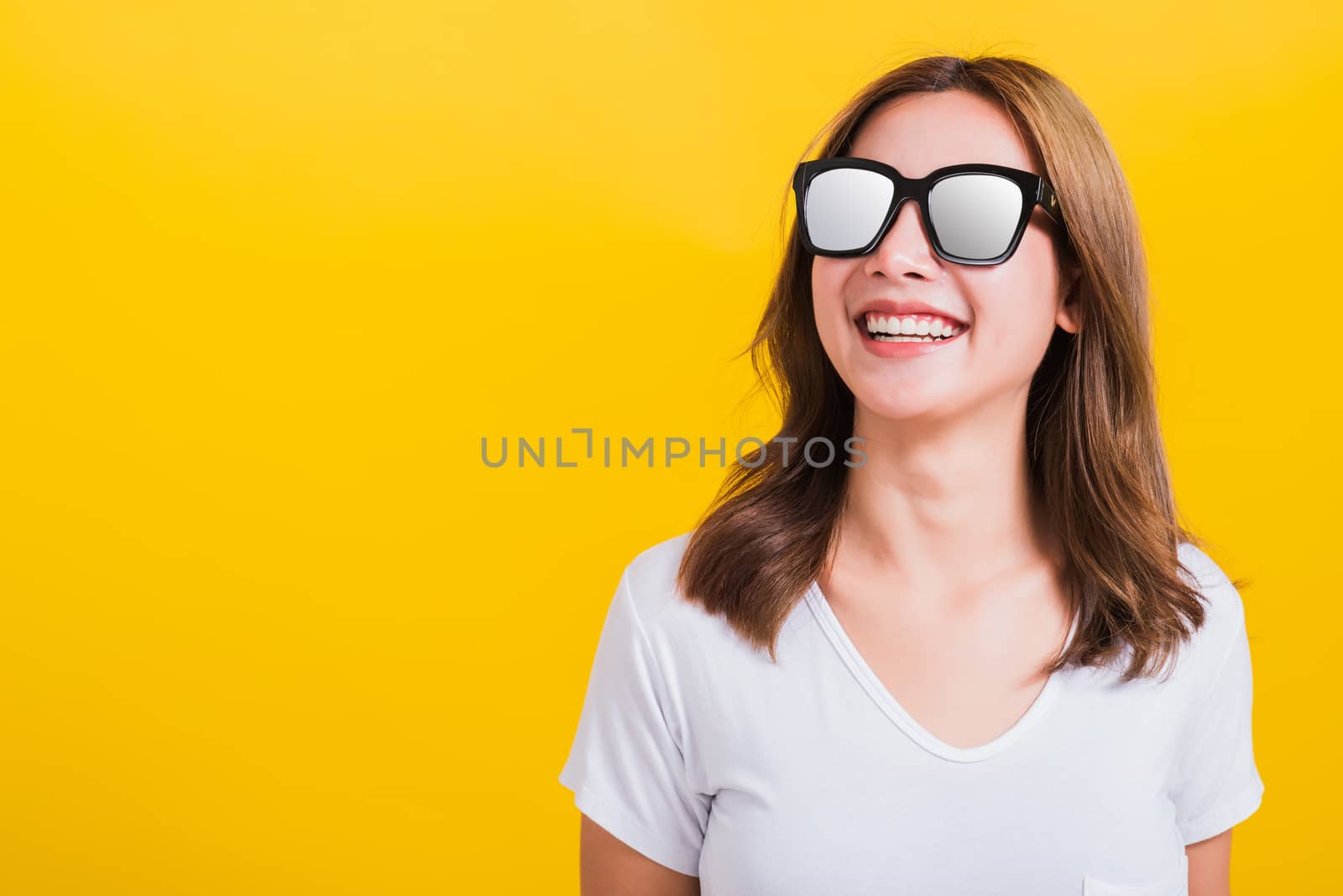 Portrait Asian Thai beautiful young woman happy smiling white teeth with sunglasses and looking side space, studio shot isolated on yellow background, with copy space