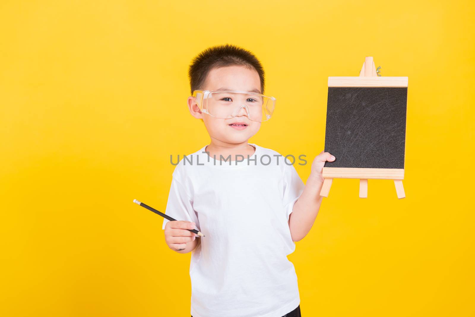 Asian Thai happy portrait cute little cheerful child boy smile he showing blackboard and looking to camera, studio shot isolated on yellow background with copy space