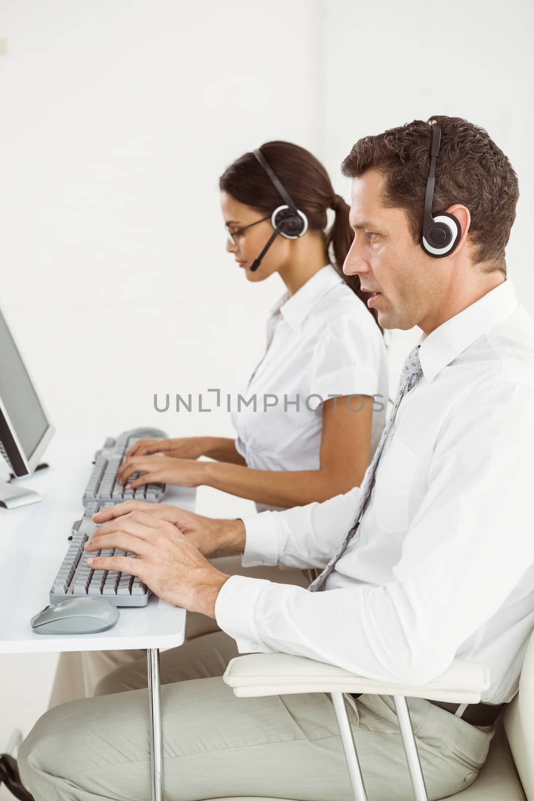 Business people with headsets using computers in office by Wavebreakmedia