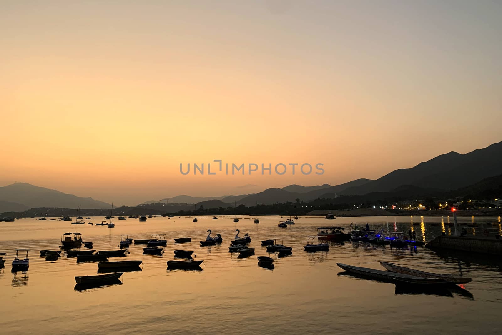 The mountain, recreational wooden boats, lake, gradient orange sky in Hong Kong countryside