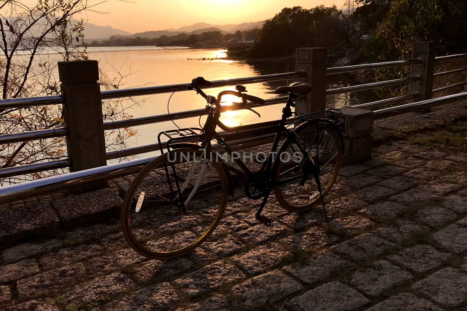 The retro bicycle, metal fence, stone floor and lake at sunset