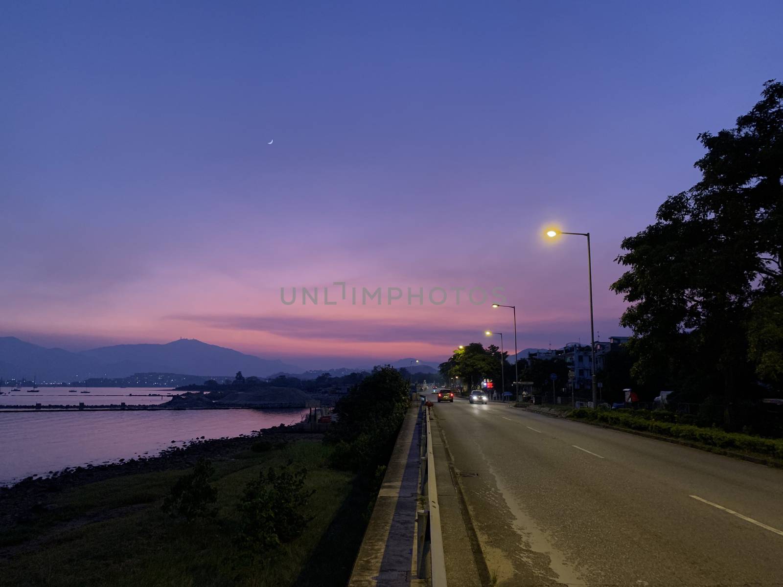 The pink and purple gradient sky, car road, bay and mountain at sunset