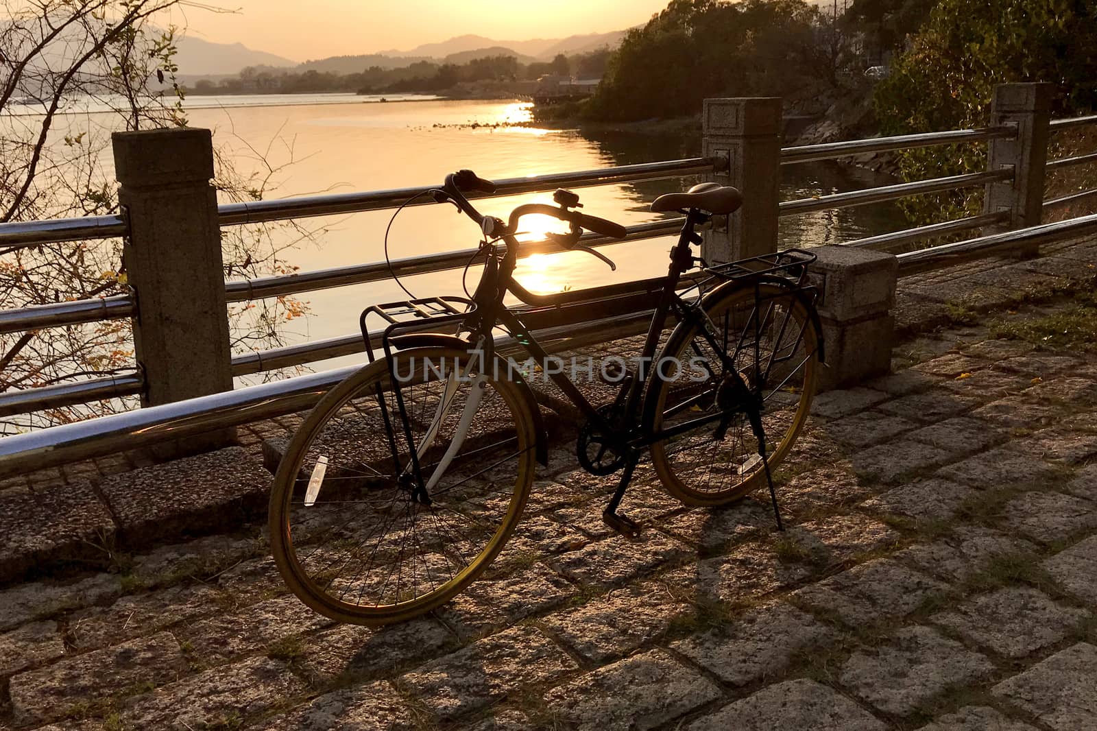 The retro bicycle, metal fence, stone floor and lake at sunset