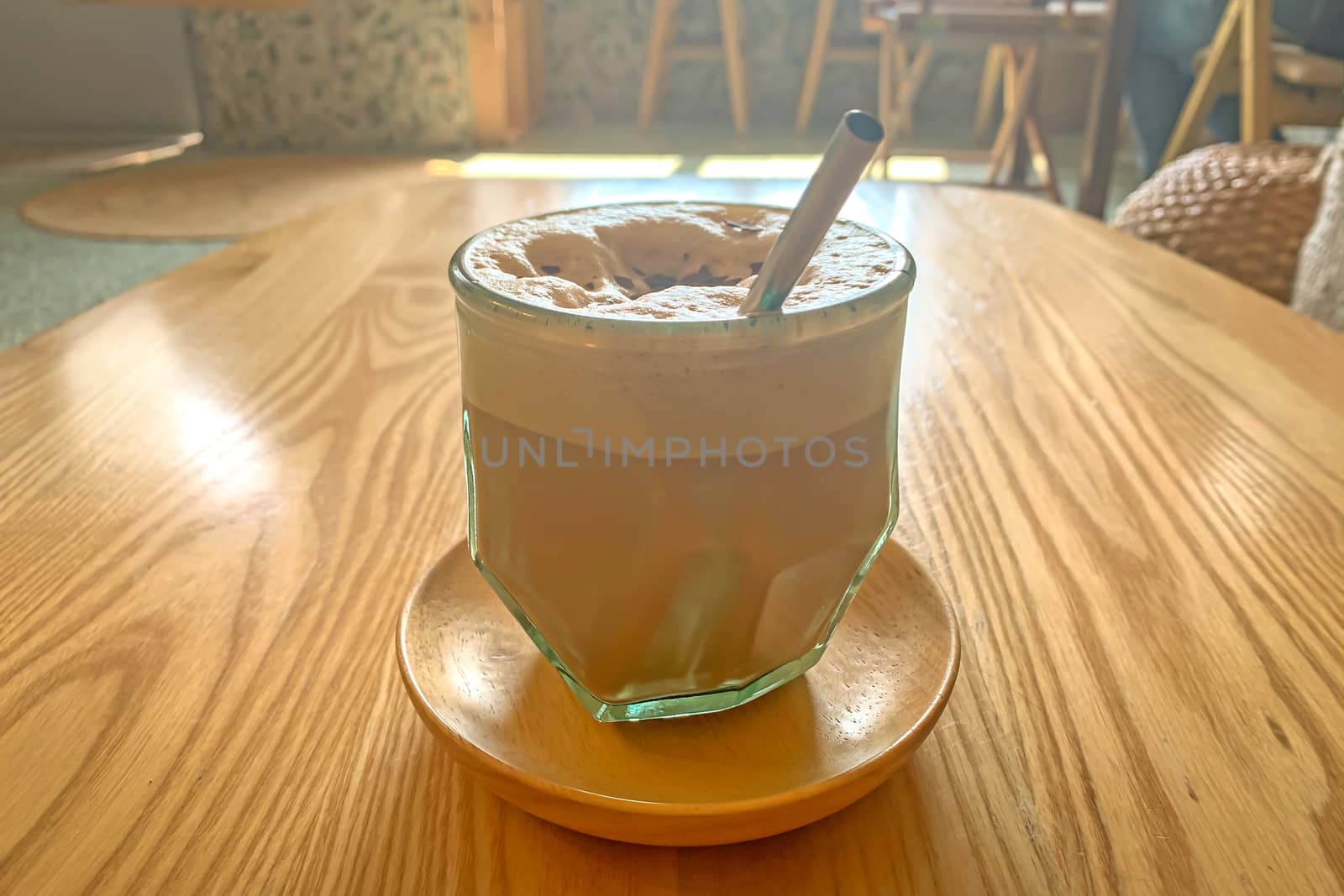 A cup of latte coffee on the wooden textured table with daylight and shadow